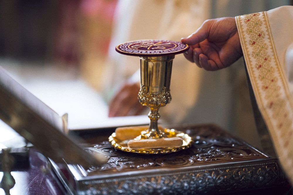 Priest lifting chalice lid during Catholic Mass ceremony on ornate altar.