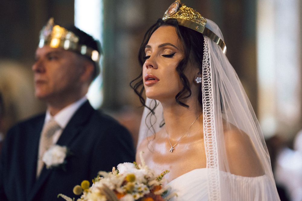Bride in white veil and floral crown holds bouquet during a church wedding ceremony.