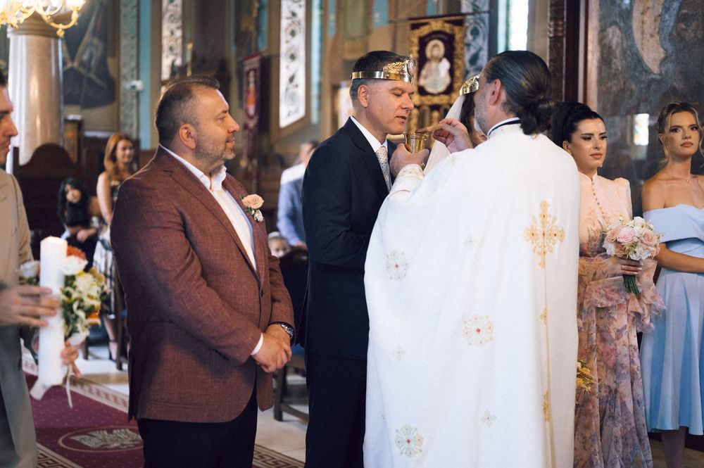 Orthodox church wedding ceremony with priest in white vestments blessing couple as guests watch.