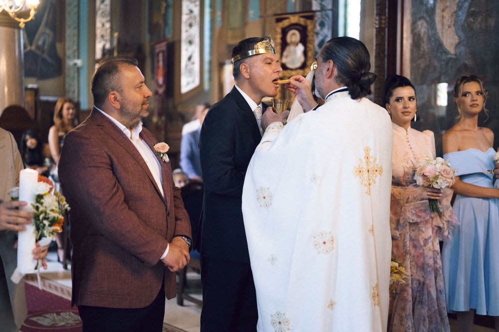 Orthodox wedding ceremony with priest blessing groom as guests watch inside ornate church.