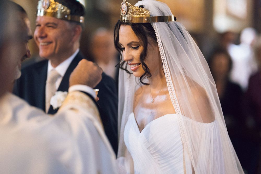 Bride wearing ornate gold crown and white veil smiles during traditional church wedding ceremony.