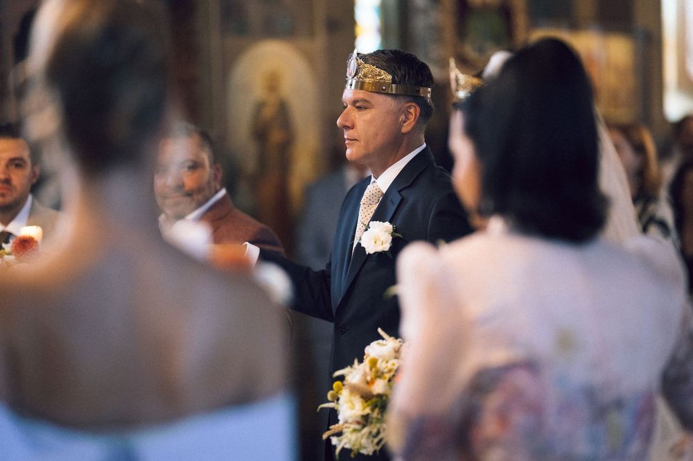 Groom wearing a crown during a Greek Orthodox wedding ceremony in a church.