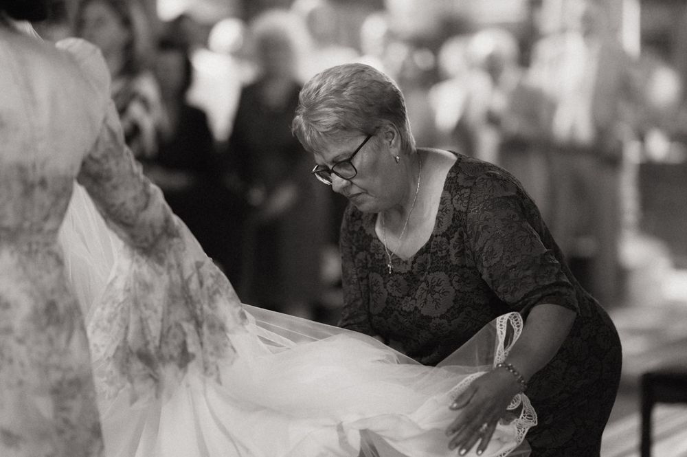 Black and white photo of a woman adjusting a bride's wedding dress train at a ceremony.