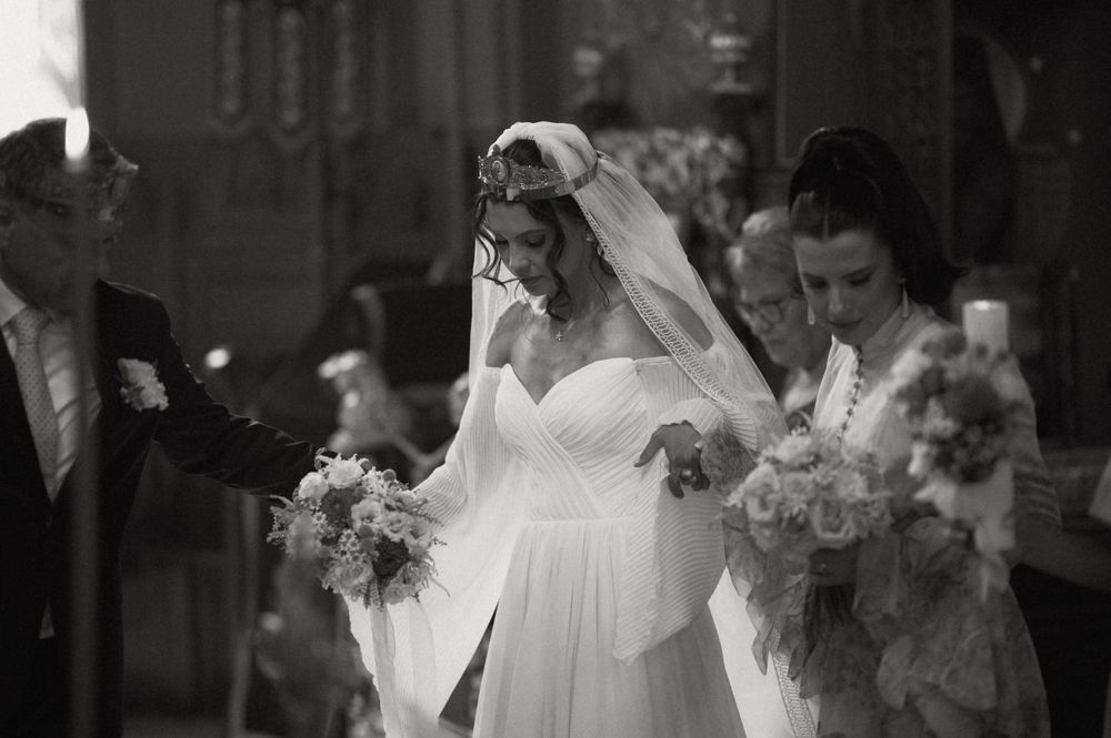 Black and white wedding photo of bride in white gown and veil walking down aisle with bouquet.
