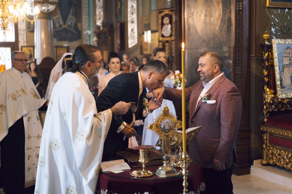 Orthodox priest performing a religious ceremony with guests in an ornate church during a formal service.