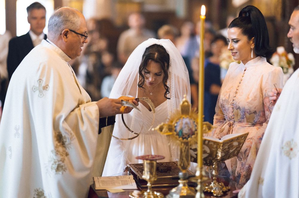 Bride in white veil receives blessing from priest during Orthodox Christian wedding ceremony in ornate church.