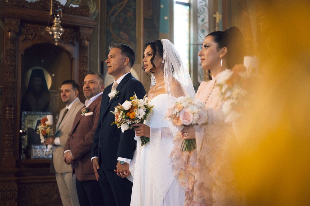 Bride and groom standing at church altar during Orthodox wedding ceremony with guests and golden icons in background.