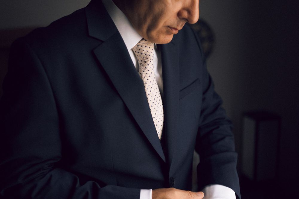 Man in dark suit adjusting cufflinks, wearing white shirt and polka dot tie, professional business attire.