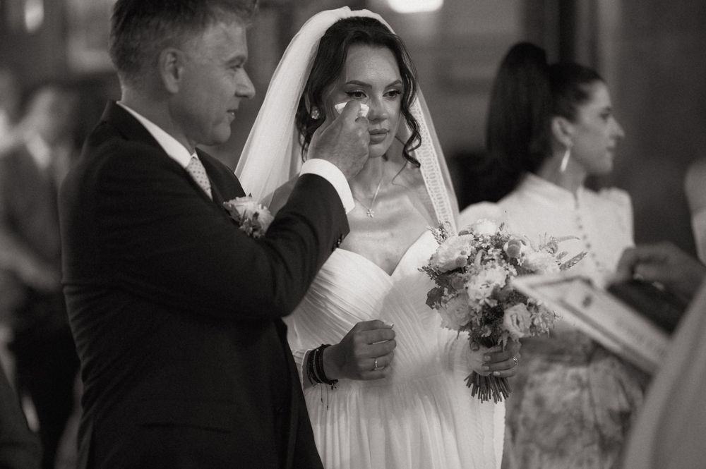 Black and white wedding photo of a groom tenderly wiping tears from his bride's cheek as she holds a bouquet.