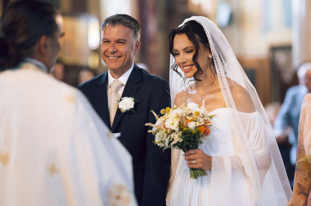 Bride in white gown and veil holds bouquet beside groom in church wedding ceremony.