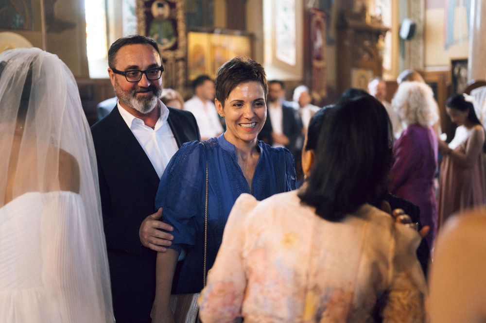 Guests smiling and conversing inside a church during a wedding ceremony, with a bride in a veil visible.