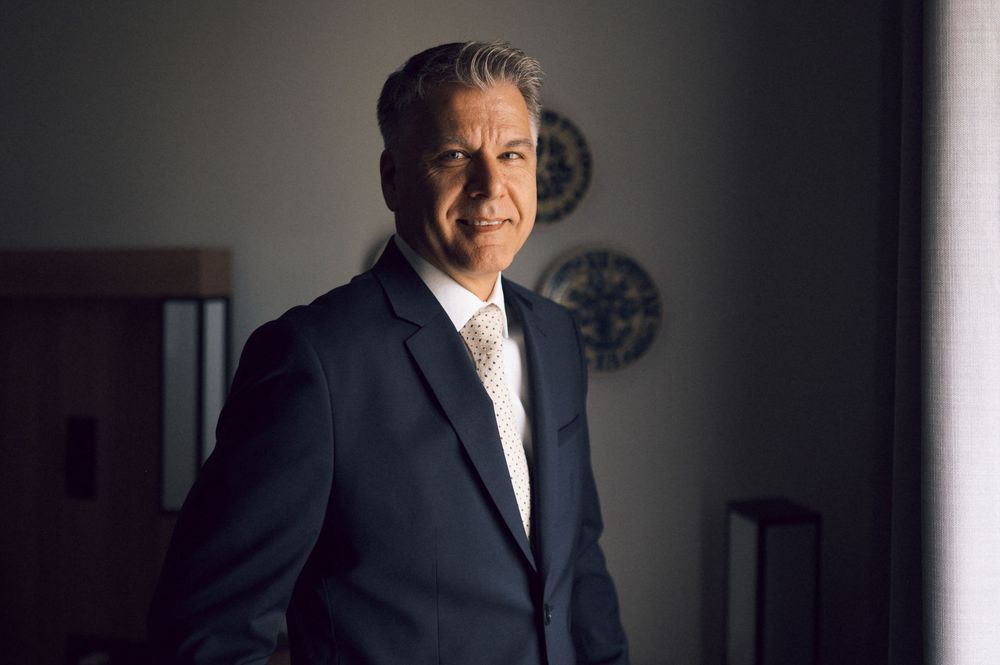 Professional businessman in dark suit and tie posing confidently in modern office setting.