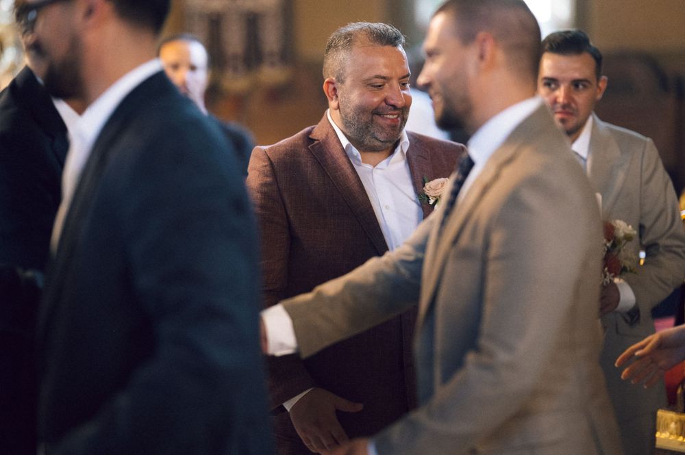 Men in suits smiling and shaking hands at a wedding ceremony indoors.