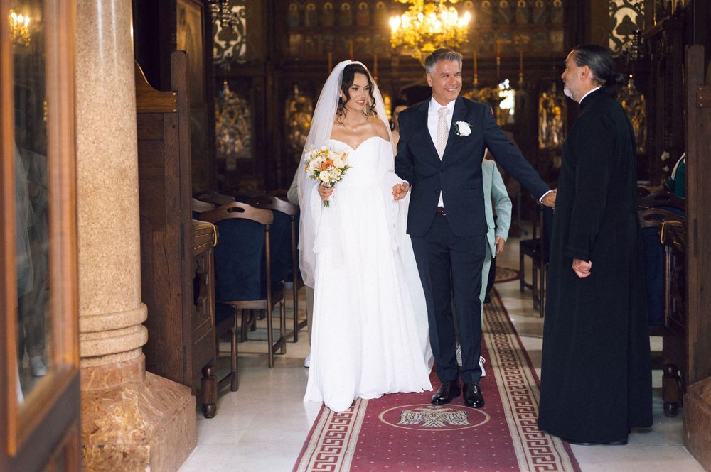 Bride in white gown and veil walks down church aisle with groom in tuxedo during elegant wedding ceremony.