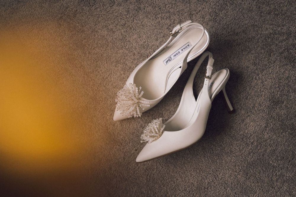 Elegant white slingback heels with floral embellishment on gray carpet, perfect bridal wedding shoes.