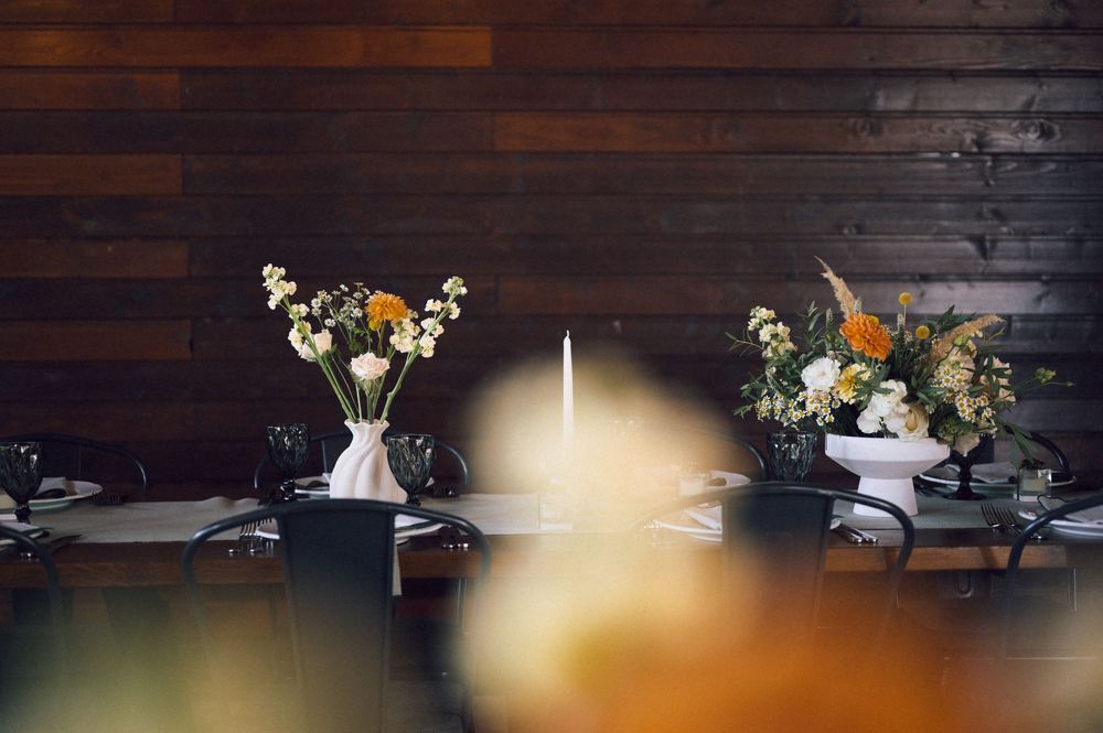 Rustic wooden wall backdrop with floral centerpieces and a white taper candle on a dark dining table.