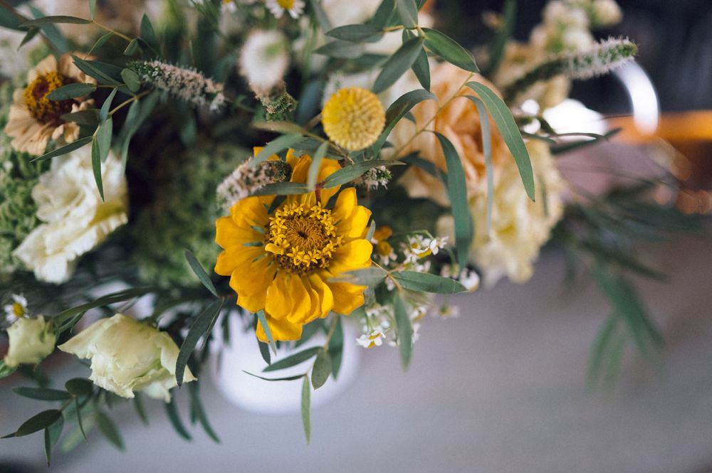 Vibrant yellow zinnia surrounded by white roses and lush greenery in an elegant floral arrangement.