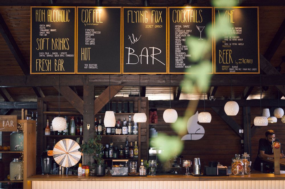 Rustic bar interior with chalkboard menus, pendant lights, and shelves of bottles at The Flying Fox Bar.