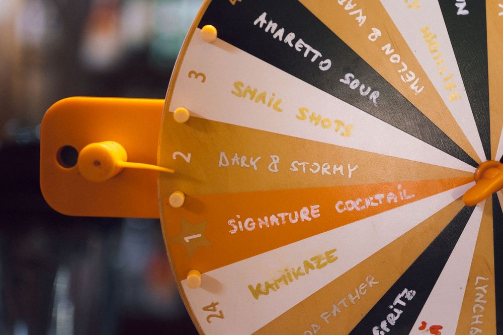 A spinning prize wheel featuring cocktail options including Amaretto Sour, Snail Shots, Dark and Stormy, and Signature Cocktail.