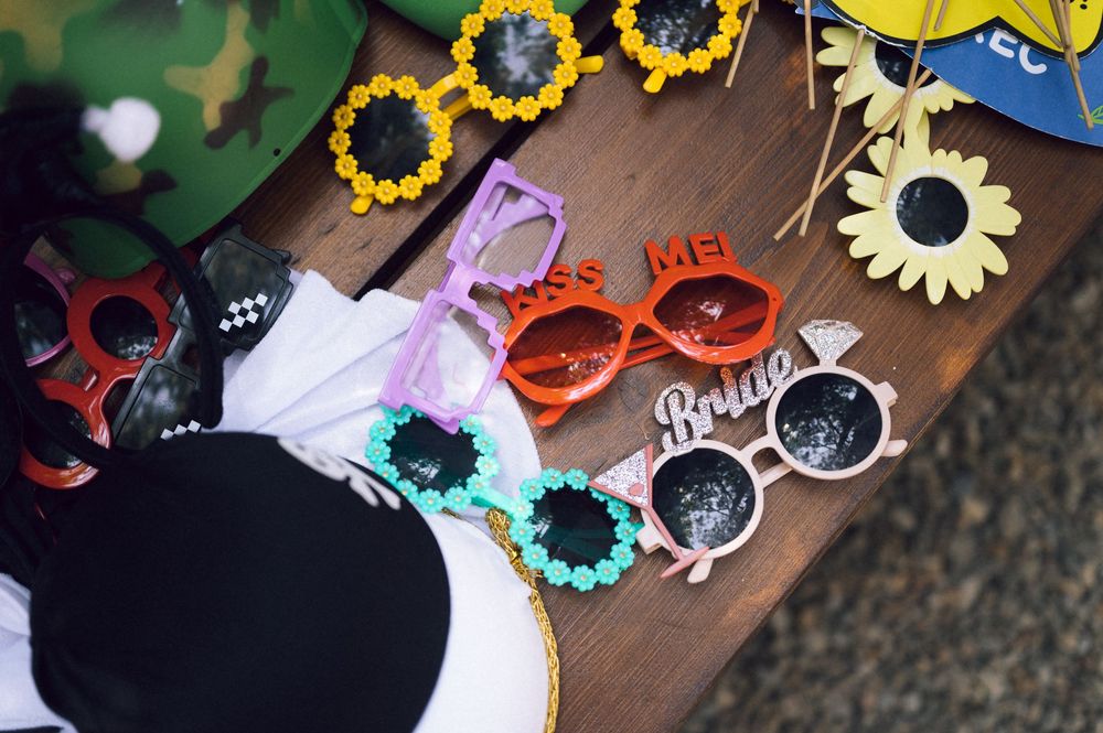 Colorful novelty sunglasses displayed on a wooden table, including bride and kiss me themed frames for a bachelorette party.