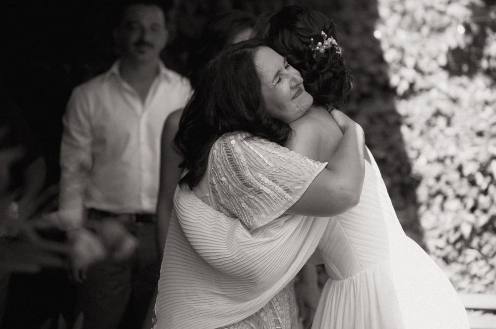 Two women share an emotional hug at a wedding ceremony in a black and white photo.