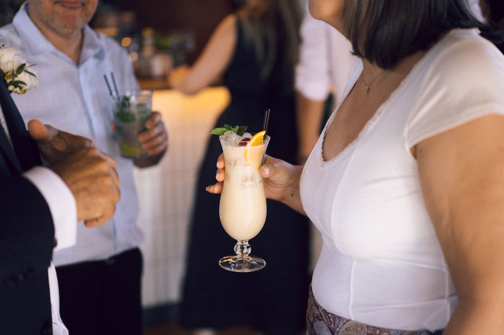 Wedding guest holds a tropical cocktail drink at an elegant reception bar.