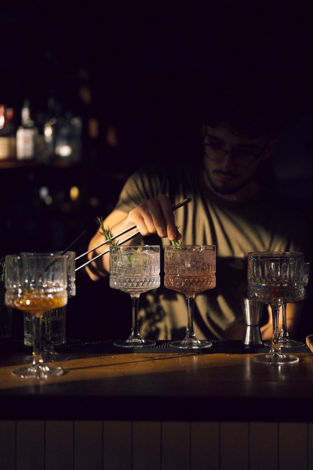 Bartender garnishing craft cocktails in elegant crystal glasses at a dimly lit bar.