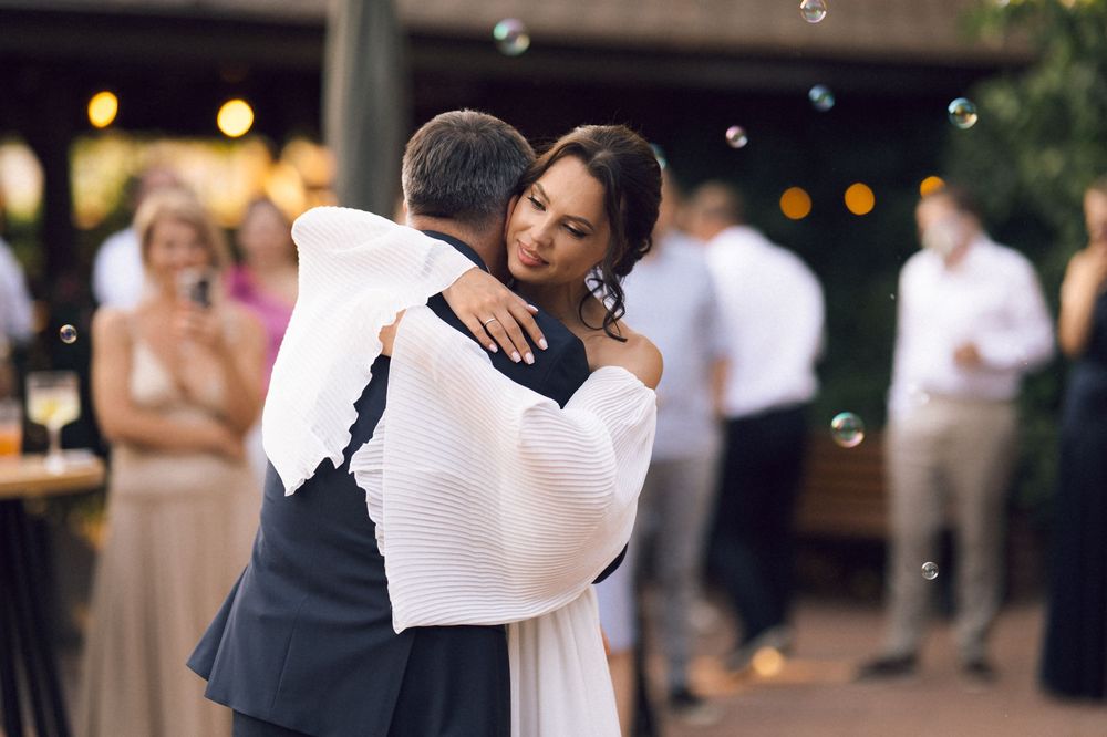 Bride and groom share an emotional first dance embrace at outdoor wedding reception with bubbles and string lights.