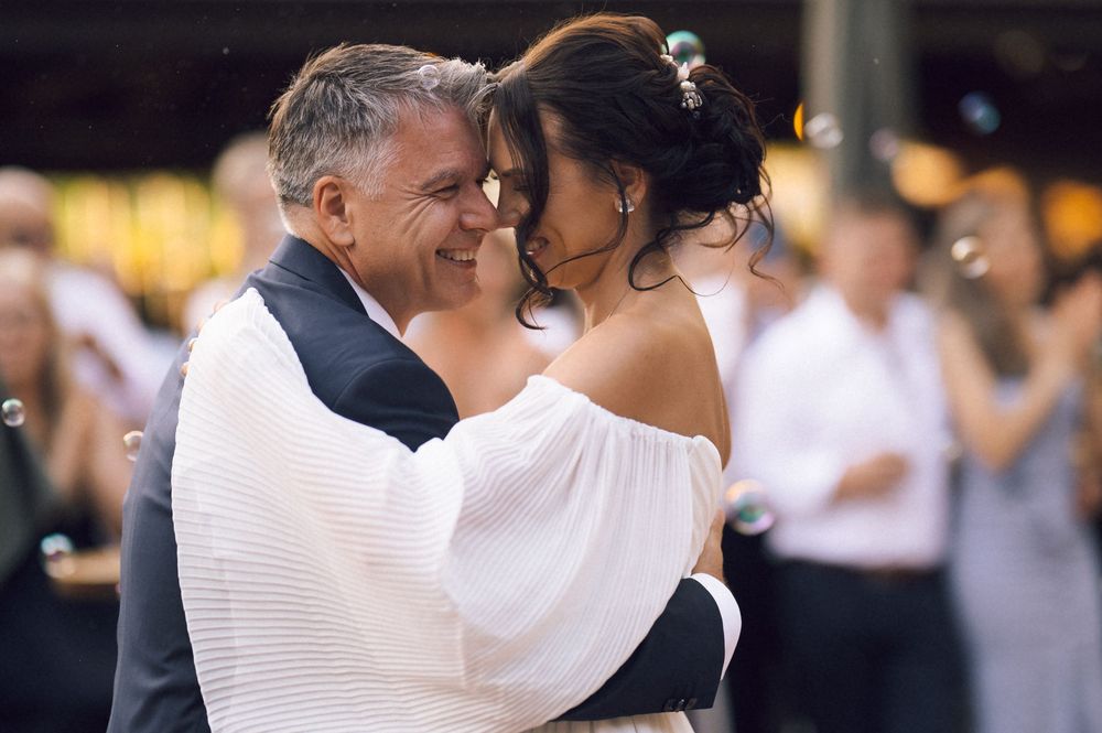 Couple sharing a romantic first dance at a wedding reception, man in suit embracing woman in white off-shoulder gown.