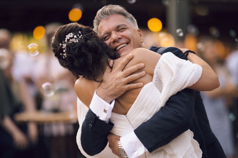 Bride and groom share a joyful embrace during their first dance at an outdoor wedding reception.