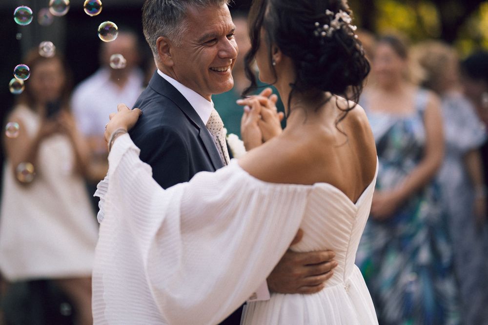 Couple sharing a romantic first dance at an outdoor wedding celebration with bubbles floating in the background.