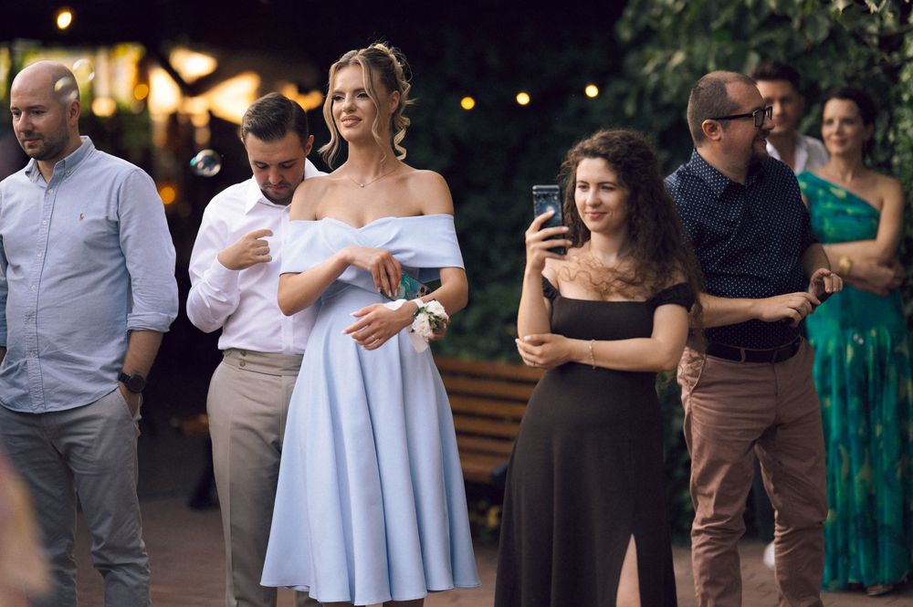 Guests in elegant attire socializing outdoors at a evening wedding reception, woman in blue dress smiling.