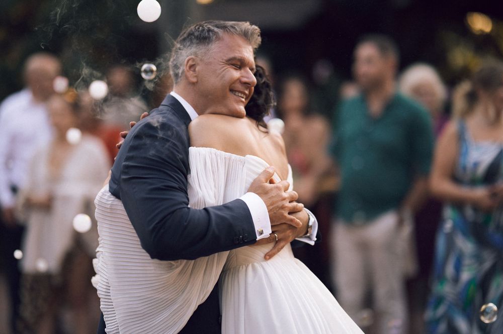 Bride and groom share their first dance at an outdoor wedding reception, surrounded by guests and floating bubbles.