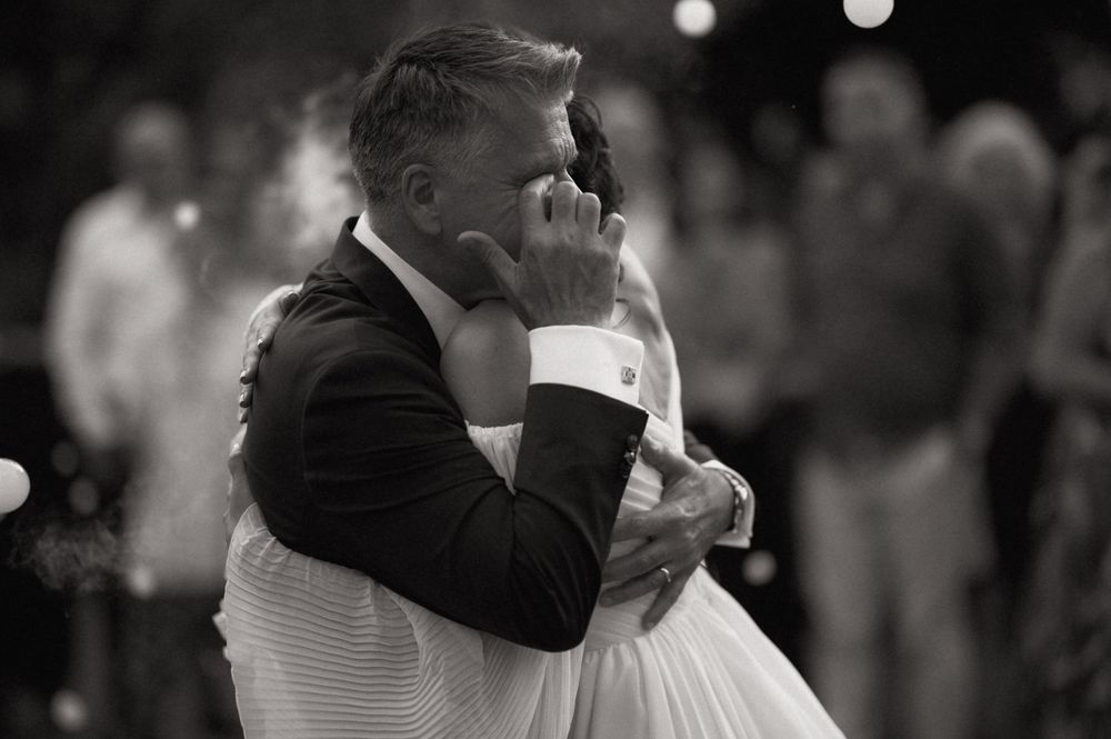 Emotional father-daughter first dance at wedding, black and white photo capturing tender embrace on dance floor.