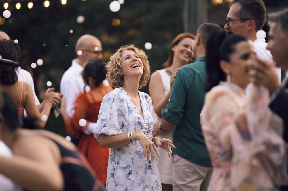 Woman in floral dress laughing joyfully while dancing at an outdoor evening party with string lights.