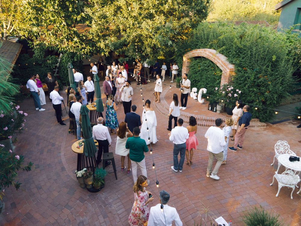 Aerial view of an elegant outdoor garden party with guests mingling on a brick patio surrounded by lush greenery.