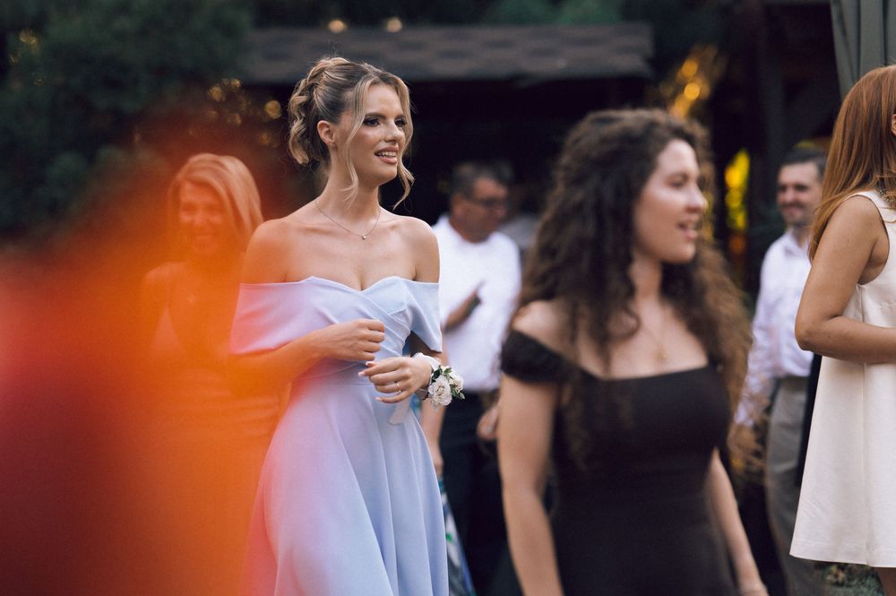 Elegant woman in light blue off-shoulder gown smiling at outdoor wedding reception event.
