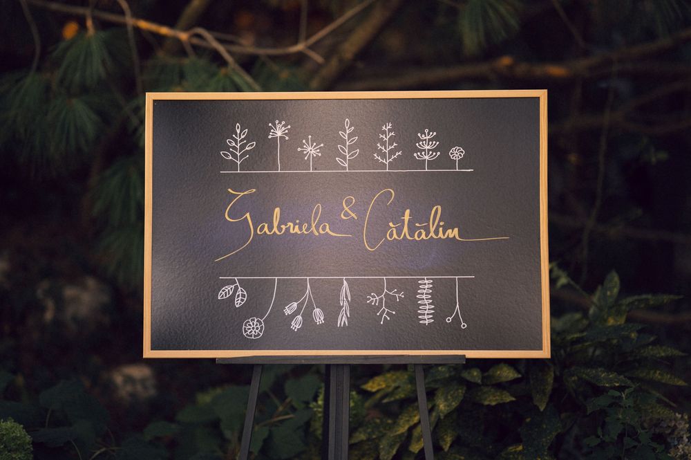 Elegant chalkboard wedding sign reading Gabriela and Catalin with floral decorations.