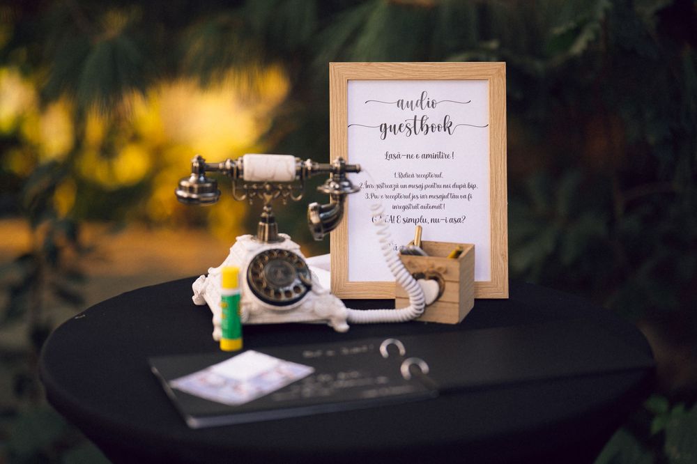 Vintage audio guestbook station with antique telephone, framed sign, and decorative items on black table at wedding.
