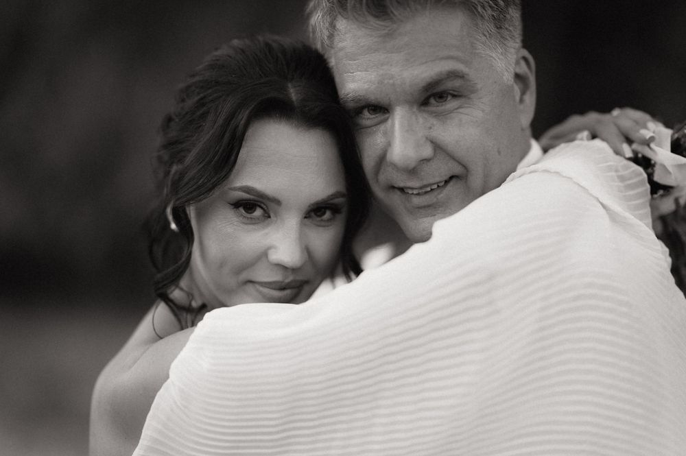 Black and white portrait of a couple embracing tenderly, woman in bridal attire leaning against mans shoulder.