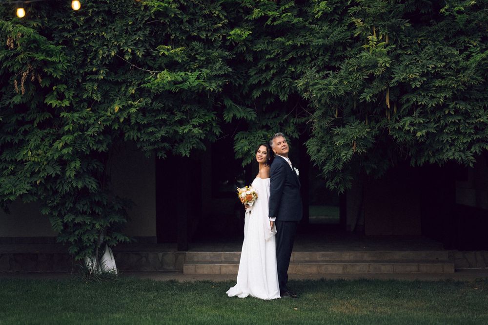 Bride and groom embracing on green lawn before ivy-covered wall in elegant outdoor wedding portrait.
