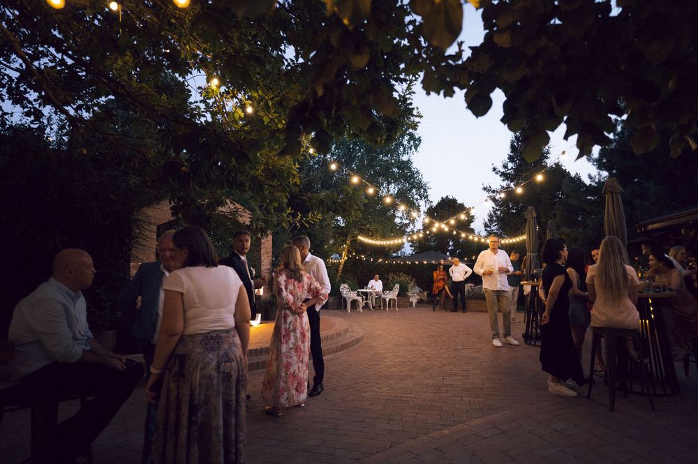 Guests mingle outdoors at a twilight garden party with string lights hanging from trees.
