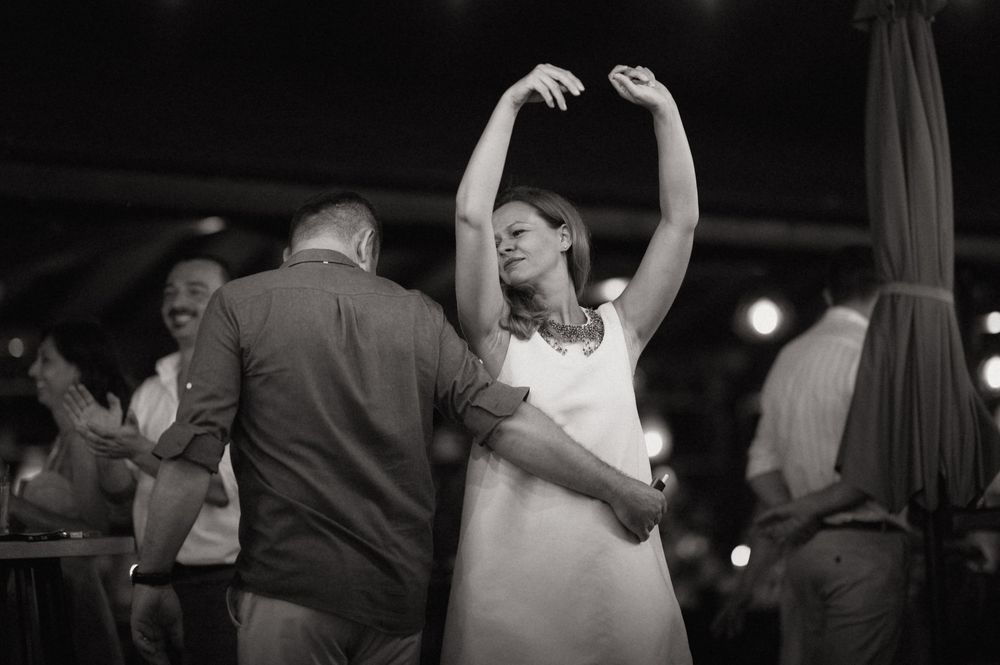 Black and white photo of a couple dancing joyfully at a wedding reception, woman with arms raised gracefully.