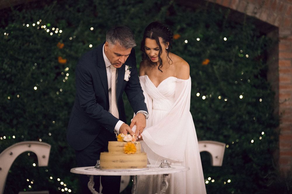 Bride and groom cutting their wedding cake outdoors at night with twinkling lights in background.