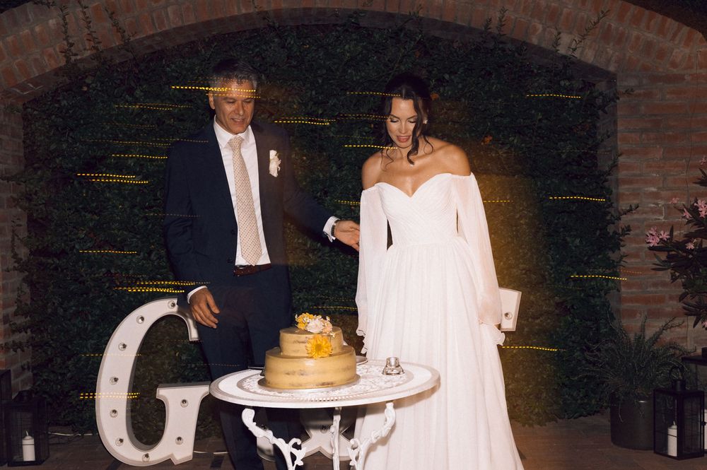 Bride and groom cutting their wedding cake at an elegant reception venue with brick arch backdrop.