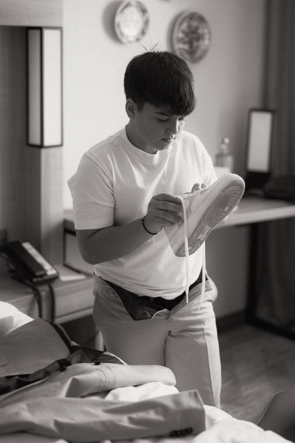 Young man in white t-shirt carefully cleaning a sneaker in a bedroom, black and white photo.