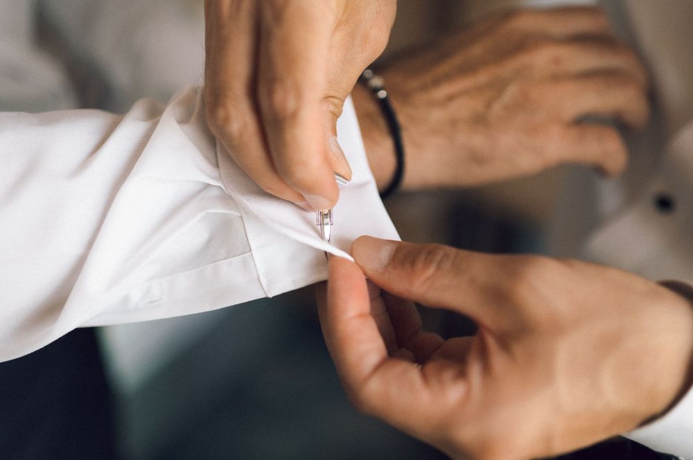 Close-up of hands fastening a white dress shirt cufflink, perfect for formal wedding or business attire styling.