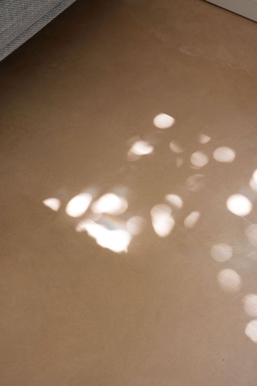 Soft dappled sunlight patterns casting circular light spots on a warm beige floor surface.