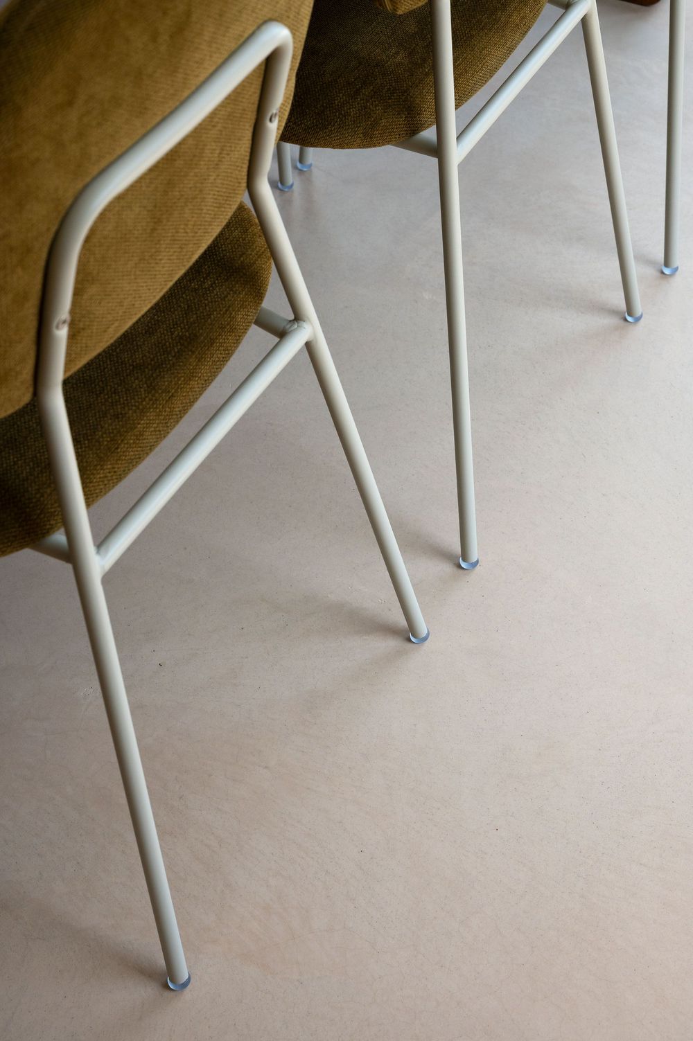 Close-up of white metal chair legs on a light beige floor with olive green upholstered seats visible above.