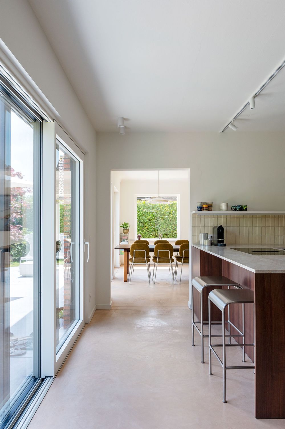 Modern open-plan kitchen with wooden island, bar stools, and sliding glass doors leading to a bright dining area with garden views.